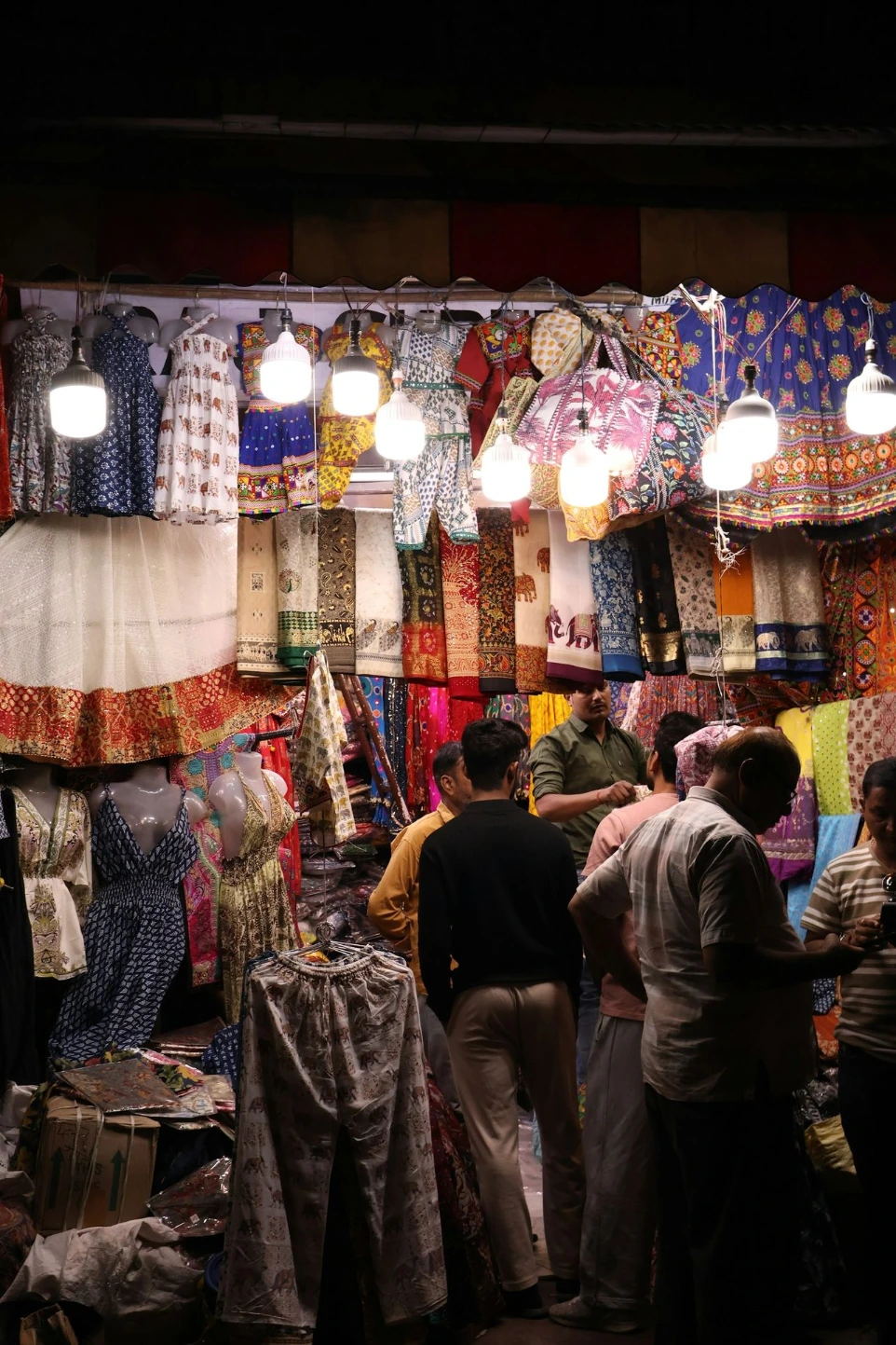 People browse colorful textiles at a busy market stall.